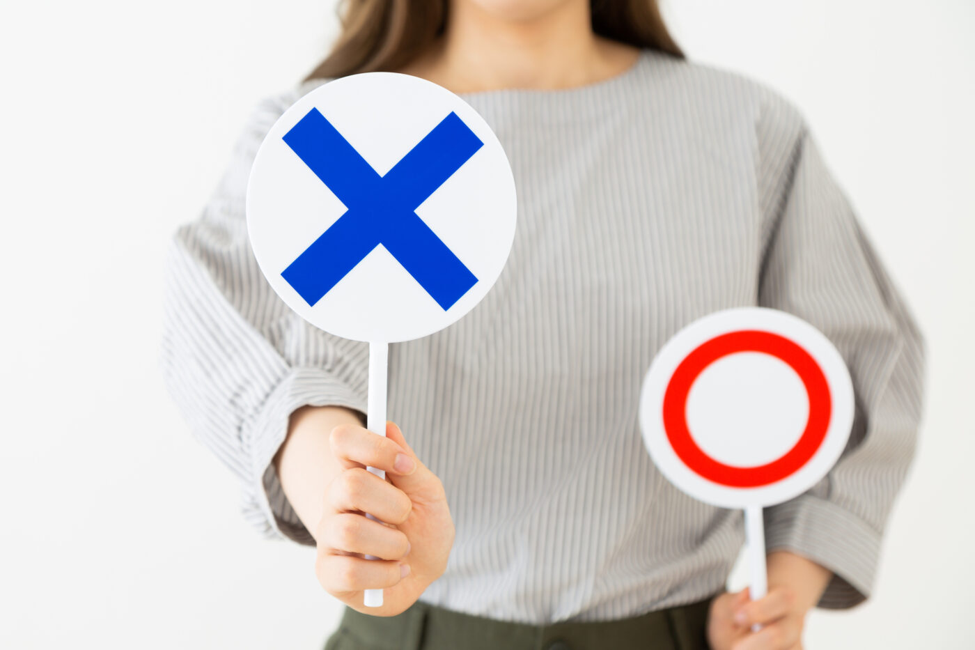 バツ(×)とマル(◯)のサインを掲げる女性の手元